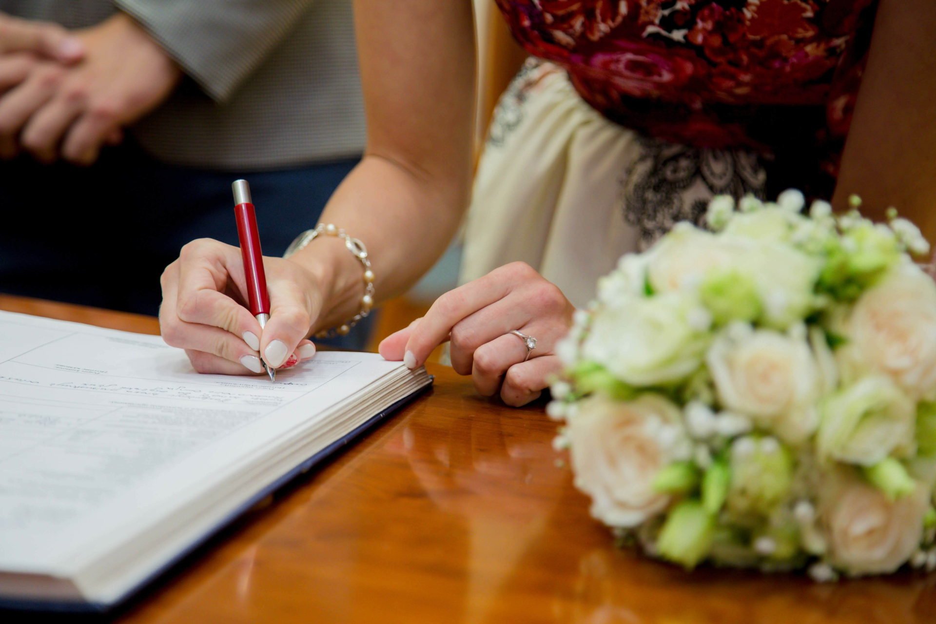 Une personne signe son acte de mariage avec un bouquet de fleurs sur la table