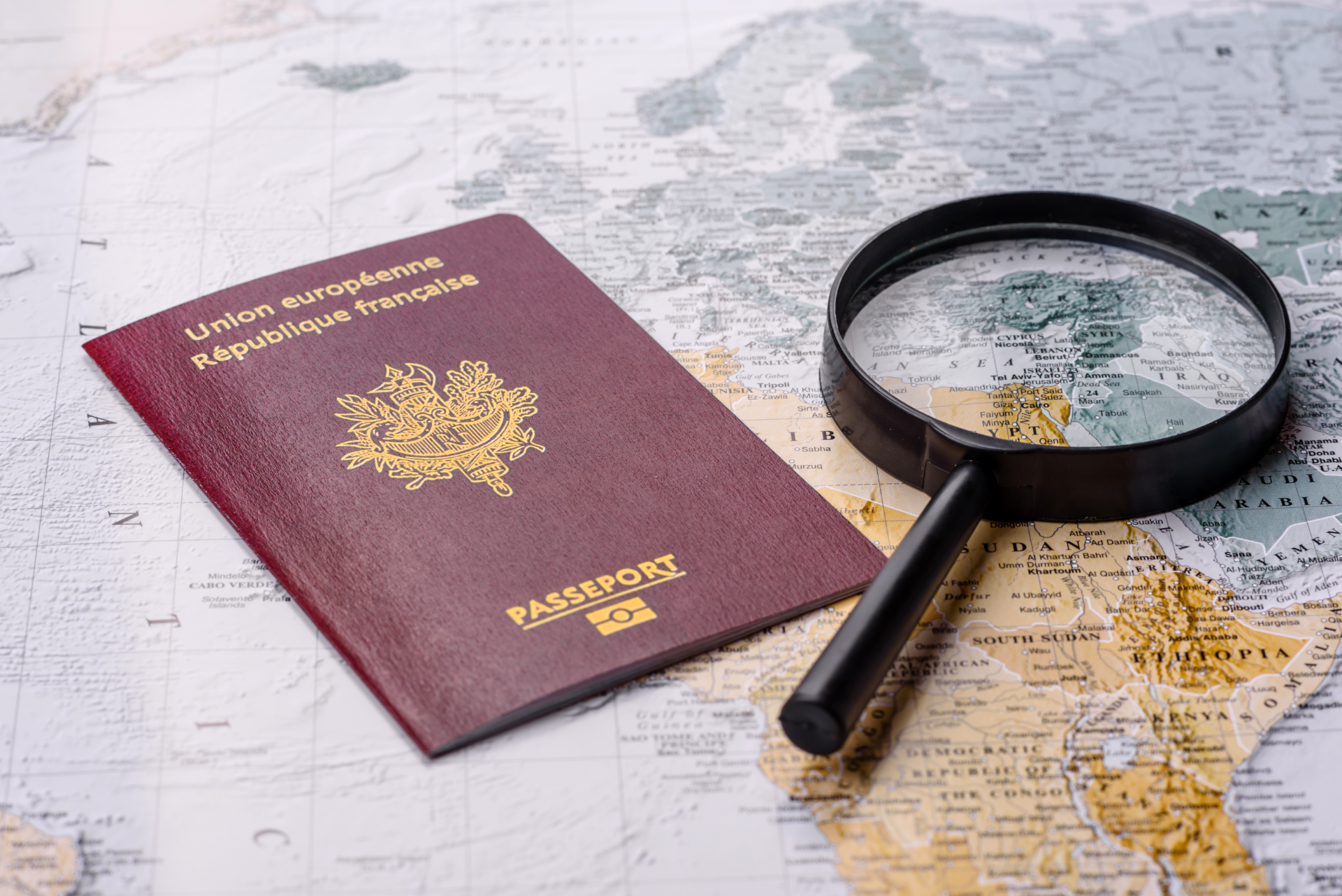 Un passeport français et une loupe posés sur une carte du monde